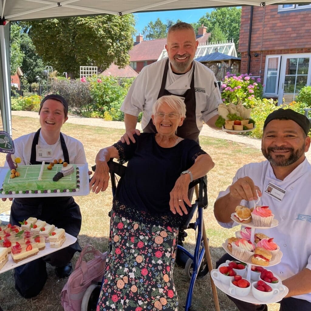 One of our Woodland Manor care home residents smiling with the kitchen team during Wimbledon celebrations.