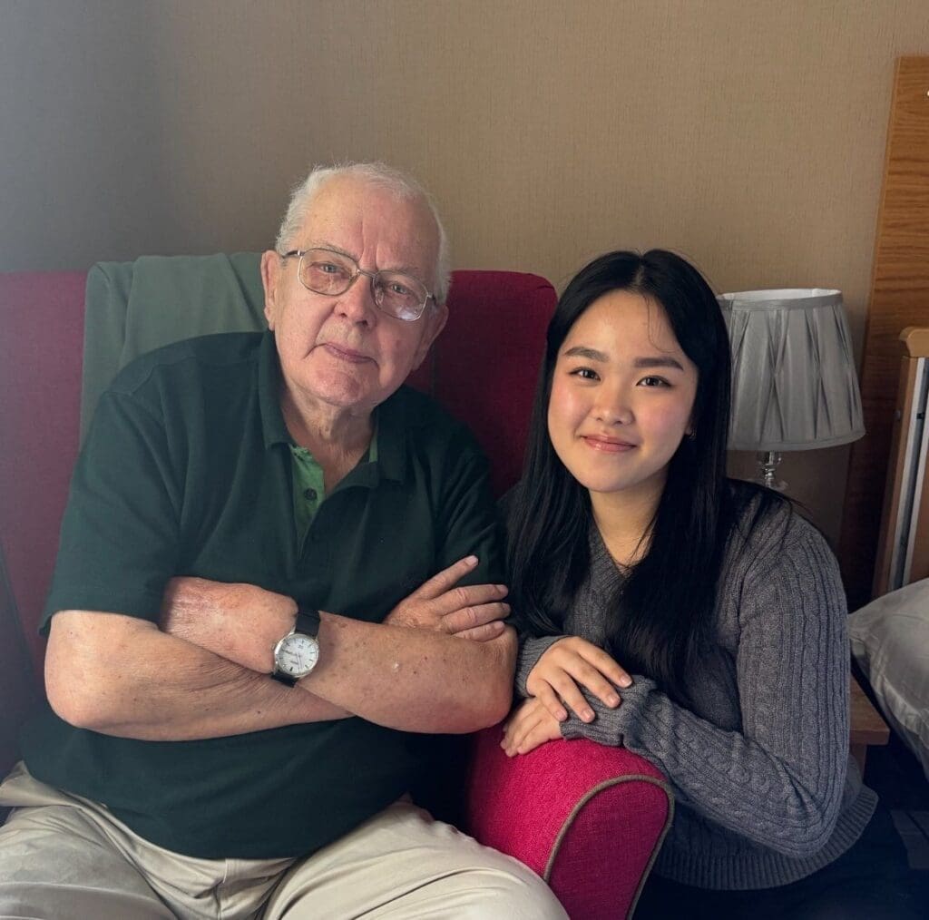 A work experience student smiling next to one of the residents at our Astbury Mere care home in Cheshire.